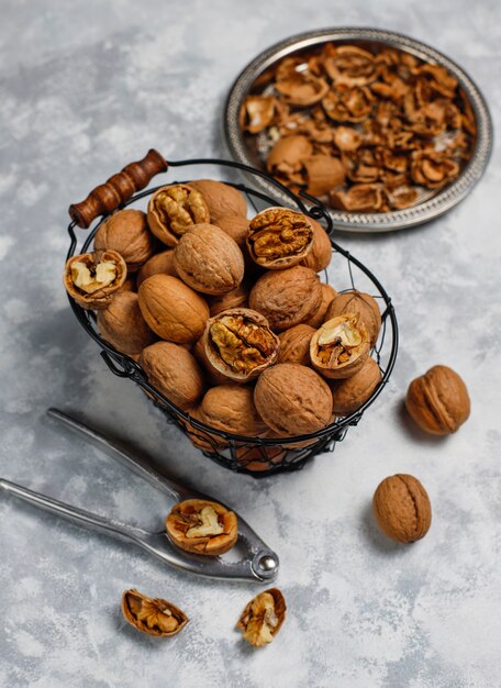 Whole walnuts in shell in food metal basket, walnut kernels. Top view on concrete 