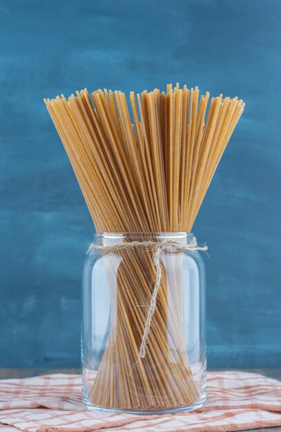 Whole wheat spaghetti in the jar, on the towel, on the marble surface. 