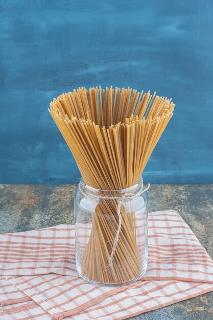 Спагетти из цельной пшеницы в банке, на полотенце, на мраморной поверхности.