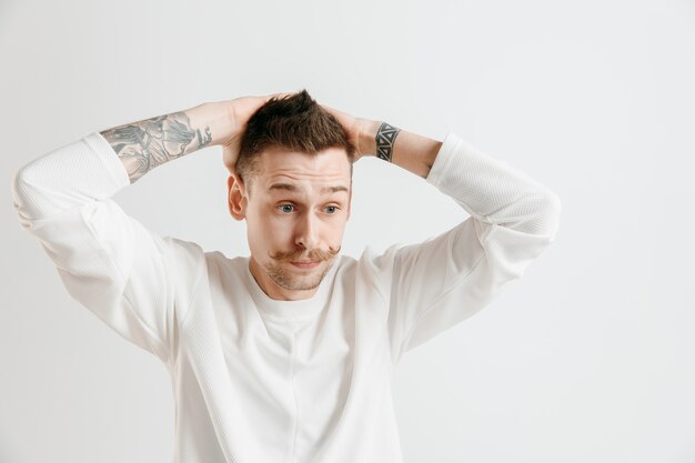 Why is that. Beautiful male half-length portrait isolated on gray studio backgroud. Young emotional surprised, frustrated and bewildered man. Human emotions, facial expression concept.