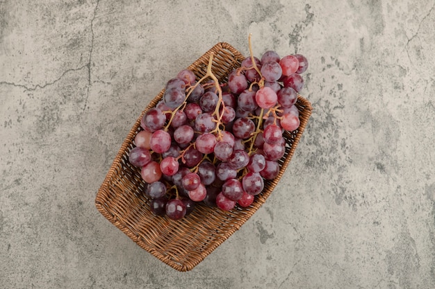 Плетеная корзина вкусного красного винограда на мраморном столе.