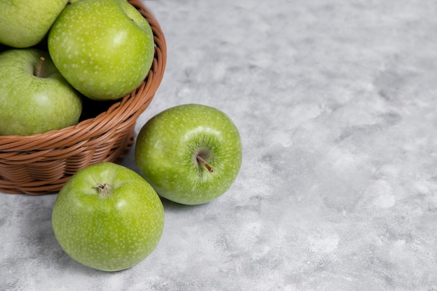 A wicker basket of fresh green apples on stone