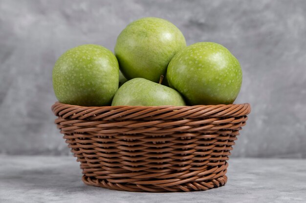 A wicker basket of fresh green apples on stone