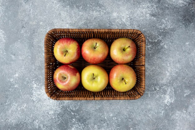 Wicker basket of fresh juicy apples on marble surface.