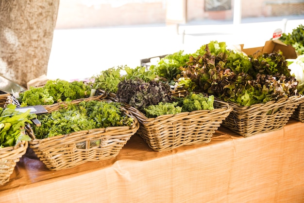 Wicker basket of fresh leafy vegetables arranged in row at market stall