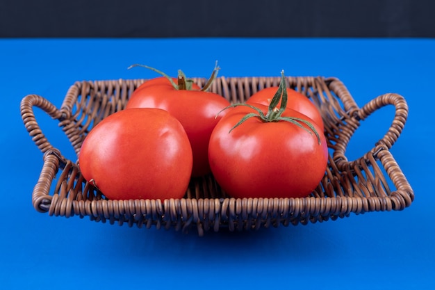 Wicker basket of fresh red tomatoes on blue surface