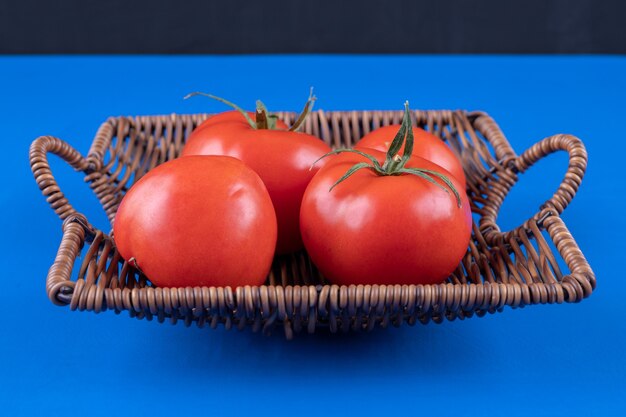 青い表面に新鮮な赤いトマトの籐のバスケット