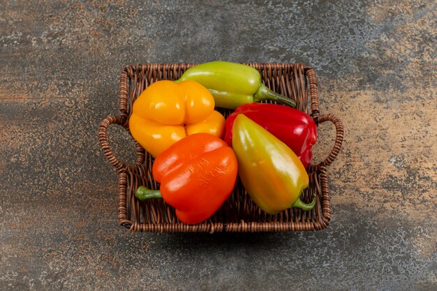 Wicker basket full of different types of peppers on the marble surface