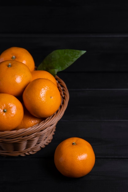 Un cesto di vimini pieno di frutta fresca di mandarino con foglie poste su un tavolo di legno scuro. foto di alta qualità