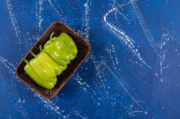 Wicker basket of green bell peppers on marble surface