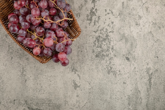 Бесплатное фото Плетеная корзина вкусного красного винограда на мраморном столе.