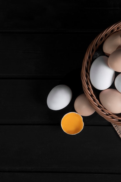 Wicker basket of raw chicken eggs on dark wooden surface. High quality photo