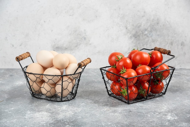 Wicker basket of raw organic eggs and red tomatoes on marble.