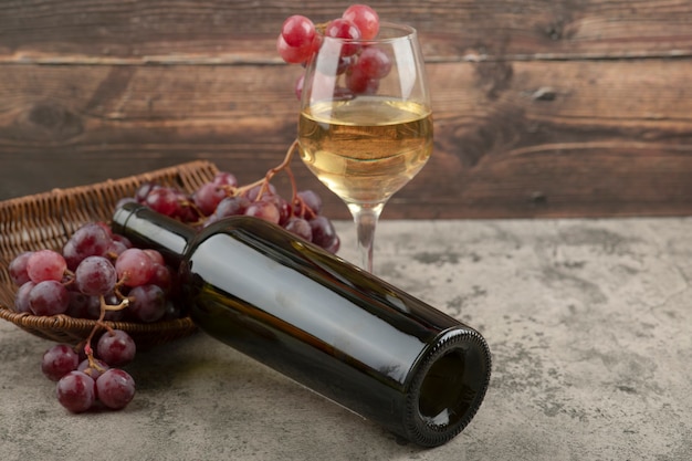 Wicker basket of red grapes with glass of white wine on marble table.