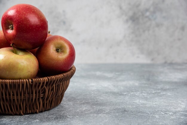 Wicker basket of red juicy apples on marble surface.