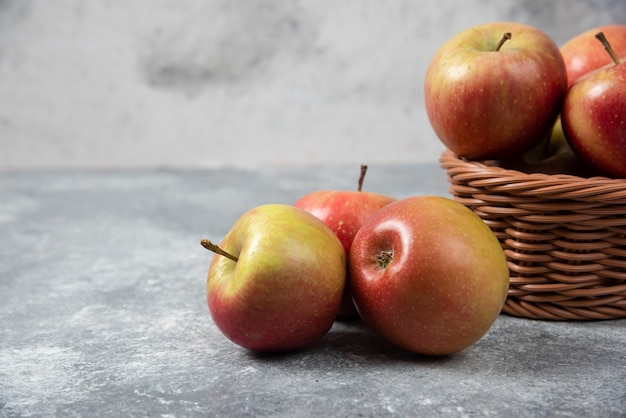 Wicker basket of red juicy apples on marble surface.