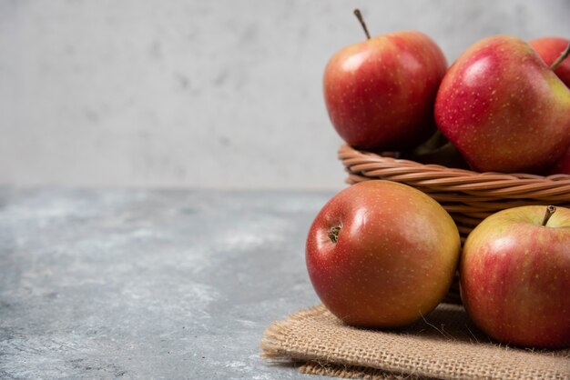 Wicker basket of ripe shiny apples on marble surface.