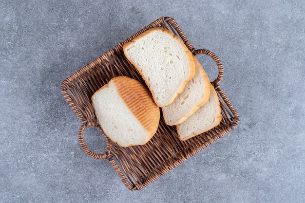 Wicker basket of sliced white bread placed on stone table.