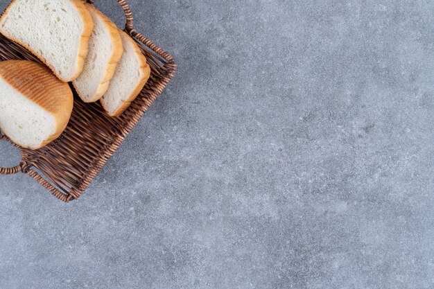 Wicker basket of sliced white bread placed on stone table. 