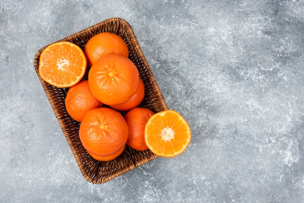 A wicker box full of juicy orange fruits on stone table .