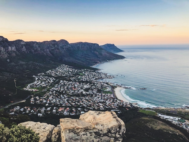 Wide aerial shot of houses on the shore of sea surrounded by mountains under a blue and pink sky