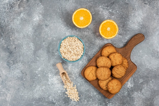 Free photo wide angle photo of homemade cookies on wooden board and oatmeal with oranges over grey surface