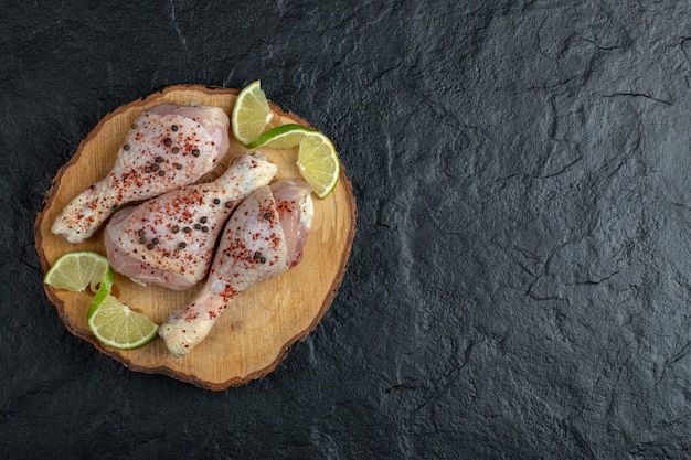 Wide angle photo off marinated raw chicken drumsticks and vegetables on black background.