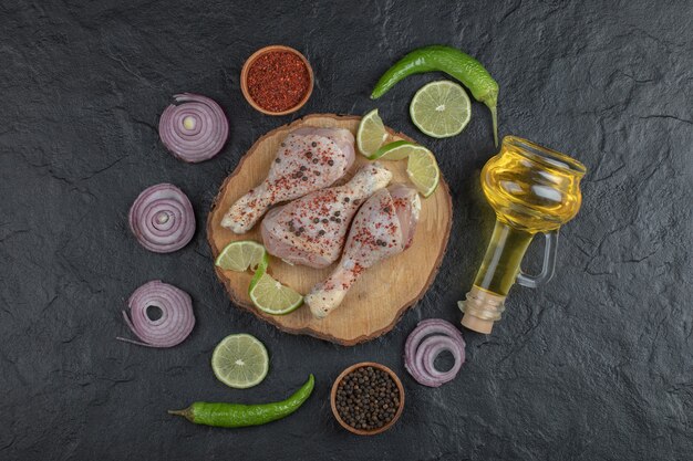 Wide angle photo of raw chicken drumsticks and vegetables on black background.