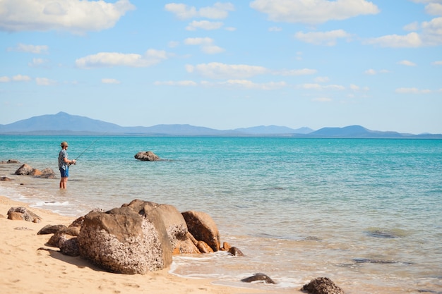 Wide angle shot of a man fishing on the beach under a clear blue sky