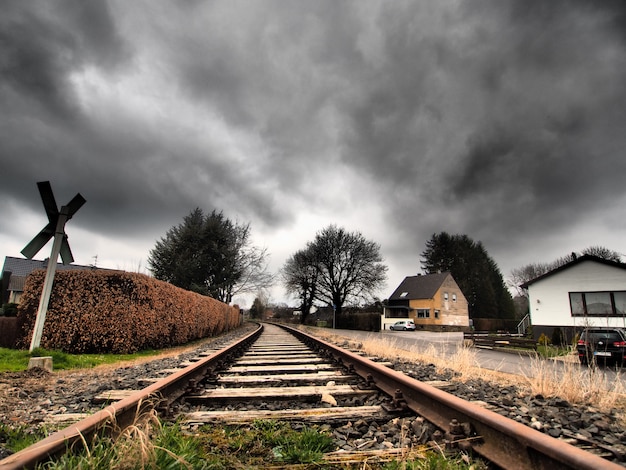 Wide angle shot of the railway tracks surrounded by trees under a clouded sky
