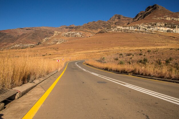 Wide angle shot of a road going on a mountain surrounded by bushes and dry grass