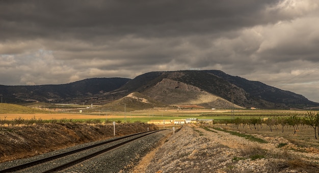 Wide angle shot of train tracks going towards a mountain under a cloudy sky