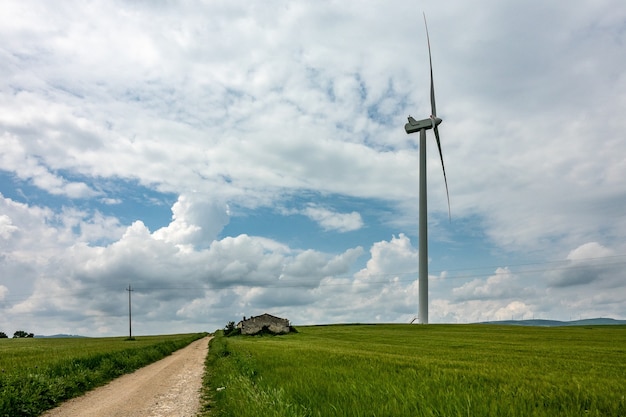 Wide angle shot of a wind fan next to a green field under a cloudy sky