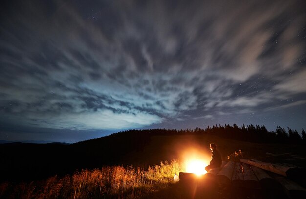 Широкоугольный вид на облачную звездную ночь в горах и человека, наслаждающегося природой
