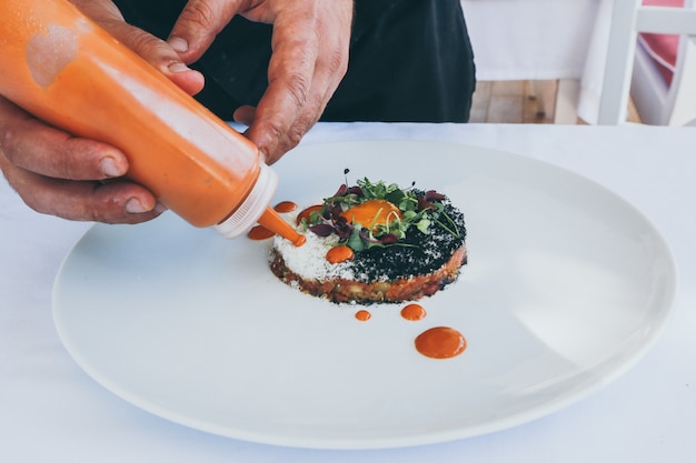 Wide closeup shot of a person pouring ketchup on a cooked meal on a white plate