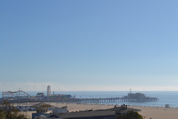 Wide distant shot of an amusement park on a dock by the sea under a clear blue sky