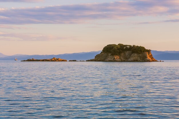 Wide landscape shot of a cliff on the body of a calm sea under a pink sky