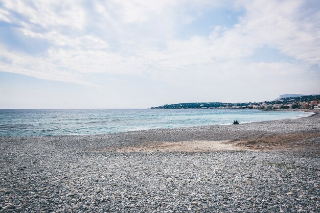 Wide landscape shot of a pebbly seashore by the sea under a clear sky