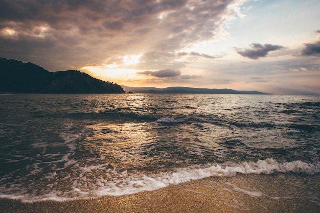 Wide landscape shot of a sea near mountains in the distance under a sky during sunset