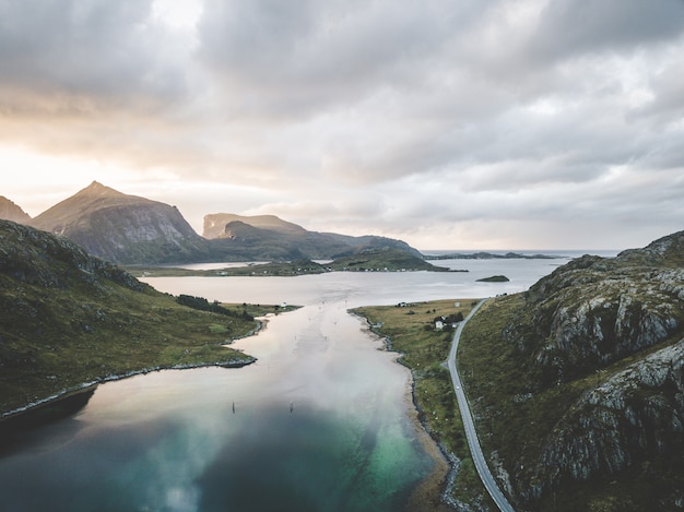 Free photo wide landscape shot of the sea surrounded by mountains under a pinkish sky with clouds