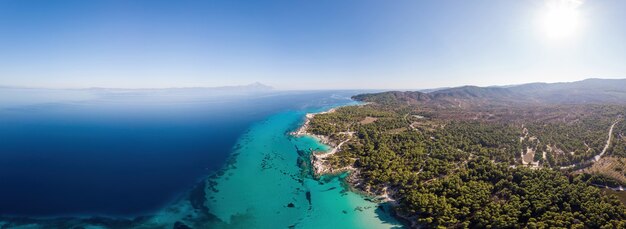Wide shot of the Aegean sea coast with blue transparent water, greenery around, pamorama view from the drone, Greece