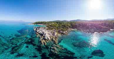 Foto gratuita ripresa a tutto campo della costa del mar egeo con acqua blu trasparente, vegetazione intorno, rocce, cespugli e alberi, colline, vista di pamorama dal drone, grecia