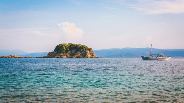 Wide shot of a boat and a green cliff on the body of water under a clear blue sky