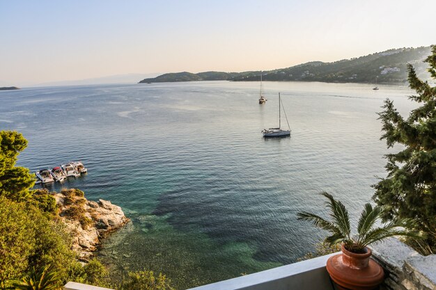 Wide shot of boats on the body of water surrounded by mountains and green plants in Skiathos, Greece