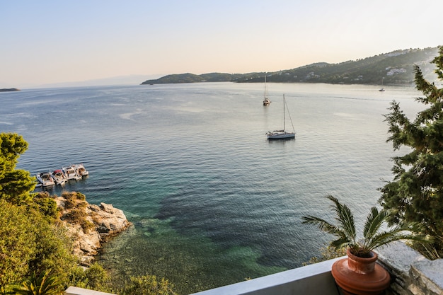 Wide shot of boats on the body of water surrounded by mountains and green plants in Skiathos, Greece