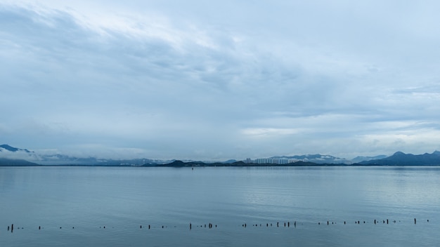 Wide shot of a calm ocean with an overlooking view of mountains on a cloudy day