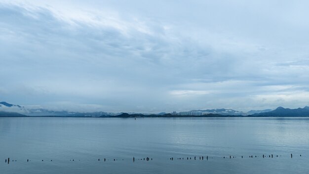 Wide shot of a calm ocean with an overlooking view of mountains on a cloudy day