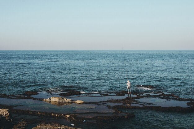 Wide shot of a fisherman standing on the shore during daytime