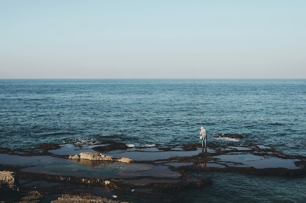 Foto gratuita panoramica di un pescatore che sta sulla riva durante il giorno