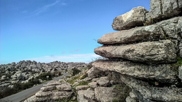 Wide shot of layers of rocks and a clear bright sky along a smooth asphalt road